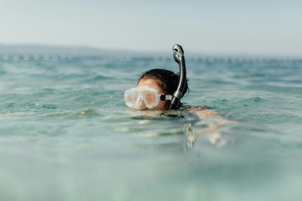 Snorkeling - femeie care poartă mască de scufundări și snorkel înot în mare într-o zi fierbinte însorită.