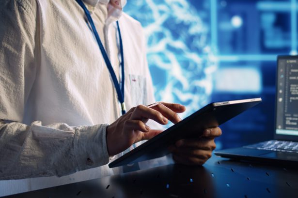 Informatician în centrul de date, rezolvând sarcini pe tabletă în timp ce rulează scripturi de programare pe terminalul laptopului.