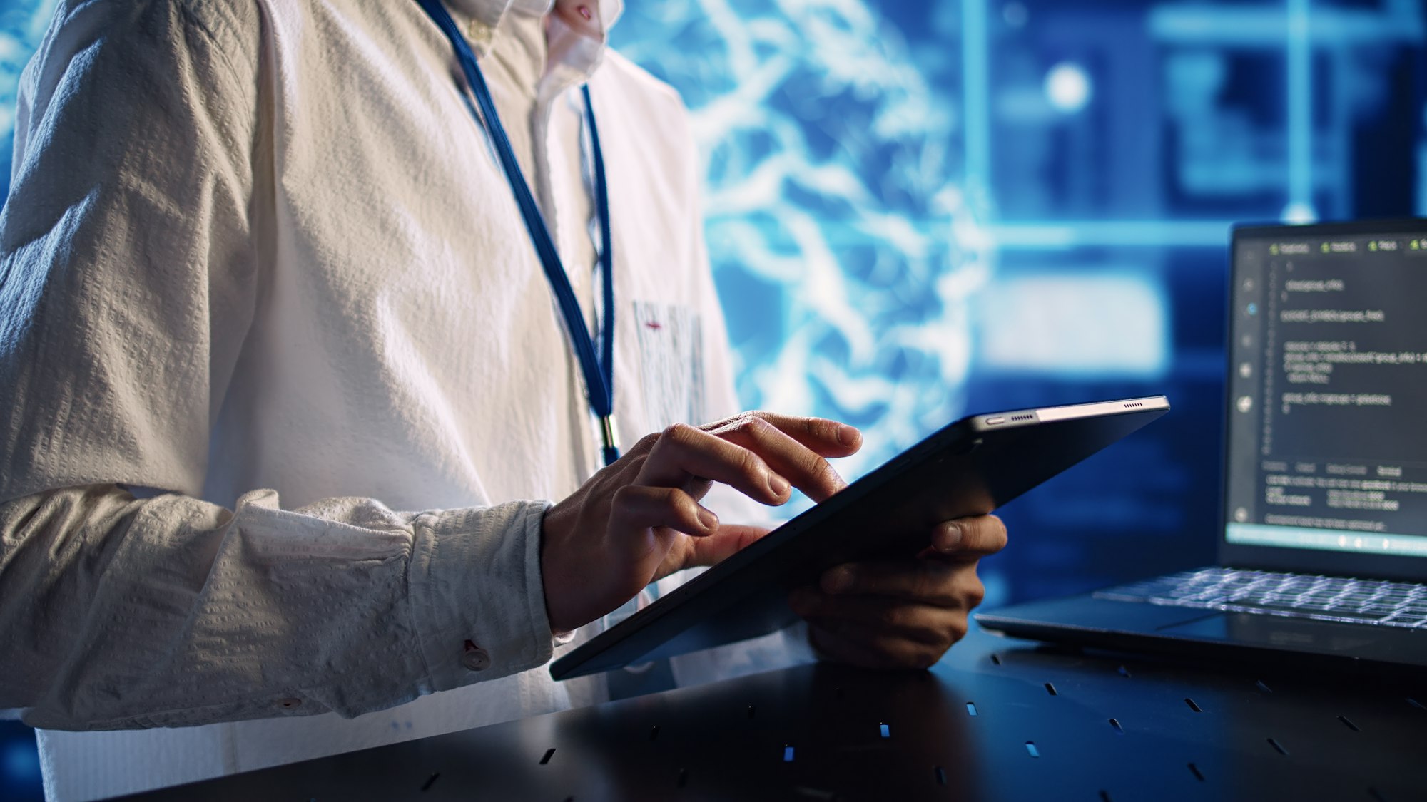 Informatician în centrul de date, rezolvând sarcini pe tabletă în timp ce rulează scripturi de programare pe terminalul laptopului.