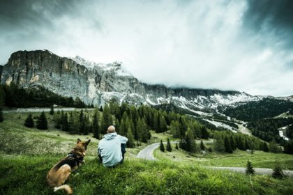 Bărbat cu câine într-o excursie rutieră la pasul Gardena din Italia, privind munții înalți.