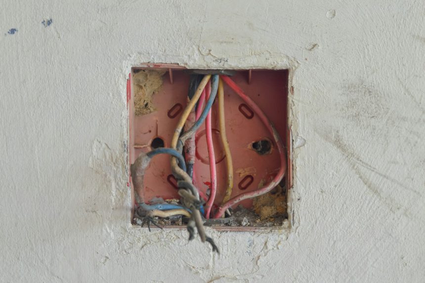 Firele, piulițele de sârmă și pânzele de păianjen aglomeran cutia de joncțiune, solicitând reorganizare și reparații electrice.