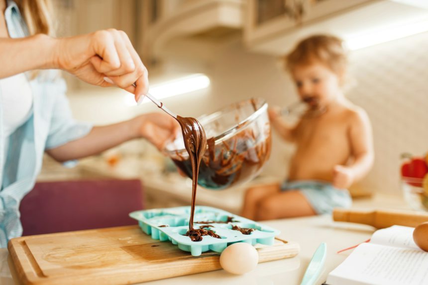 Tânăra mamă și copilul pregătesc produse de patiserie și gustă ciocolată topită.
