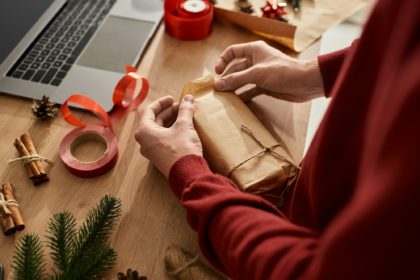 Tânărul împachetează cu grijă un cadou, înconjurat de decorațiuni și rechizite de sărbători.