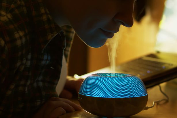 Femeia inhalează vapori aromatici din difuzorul de uleiuri esențiale în timp ce lucrează în bucătărie