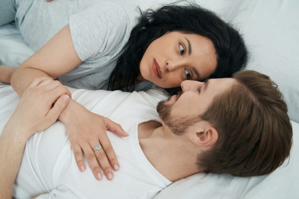 Femeie romantică întinsă lângă persoana iubită în pat și privindu-i în ochi