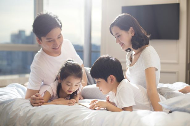 O tânără familie chineză veselă citind o carte pe pat