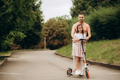 tata își învață fiica să meargă cu scuterul electric