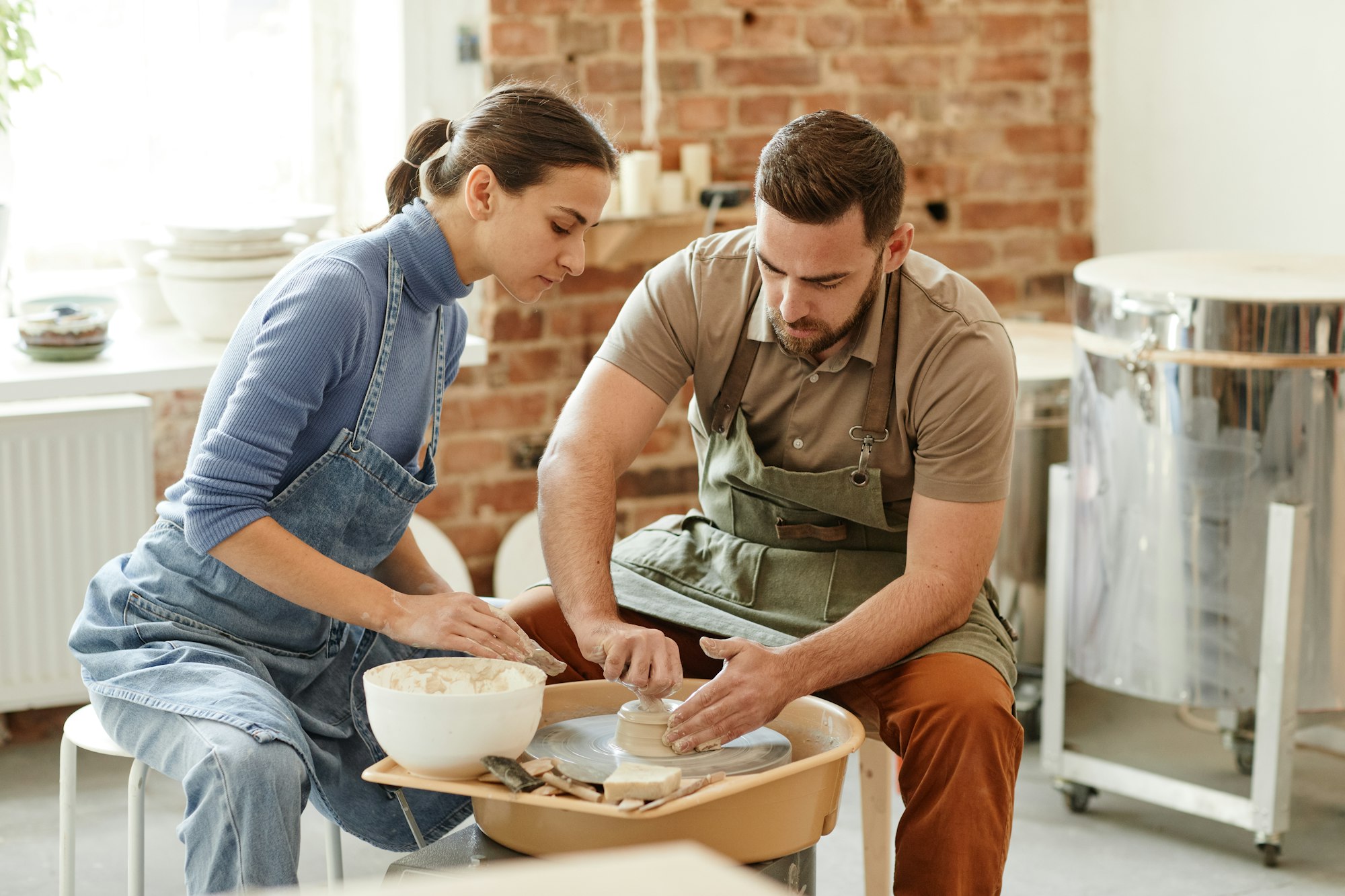 Portretul unui cuplu tânăr stând împreună lângă roata de ceramică într-un atelier de ceramică lucrată manual, spațiu de copiere
