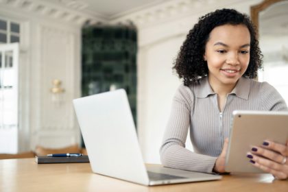 Tânăr profesionist angajat, folosind tableta alături de laptop într-un birou de acasă elegant și bine iluminat, îmbinând tehnologia și confortul.