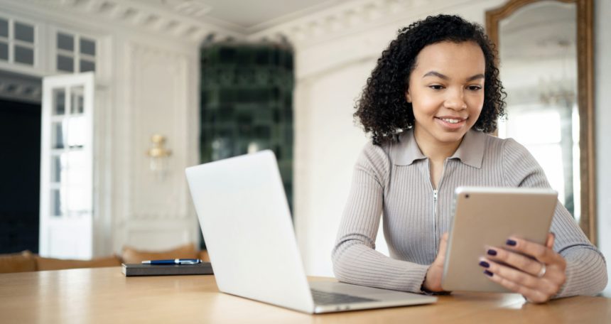Tânăr profesionist angajat, folosind tableta alături de laptop într-un birou de acasă elegant și bine iluminat, îmbinând tehnologia și confortul.