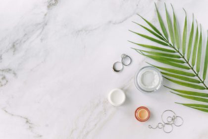 borcane mici cu cremă de față hidratantă și hrănitoare pe masă, bijuterii și frunze de palmier - concept de frumusețe și spa