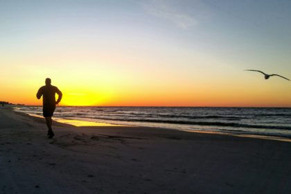 Siluetă milenar alergând pentru viața sa în sănătate și fitness pe malul mării de pe coasta golfului Floridei în Ora de aur cu păsări zburătoare.