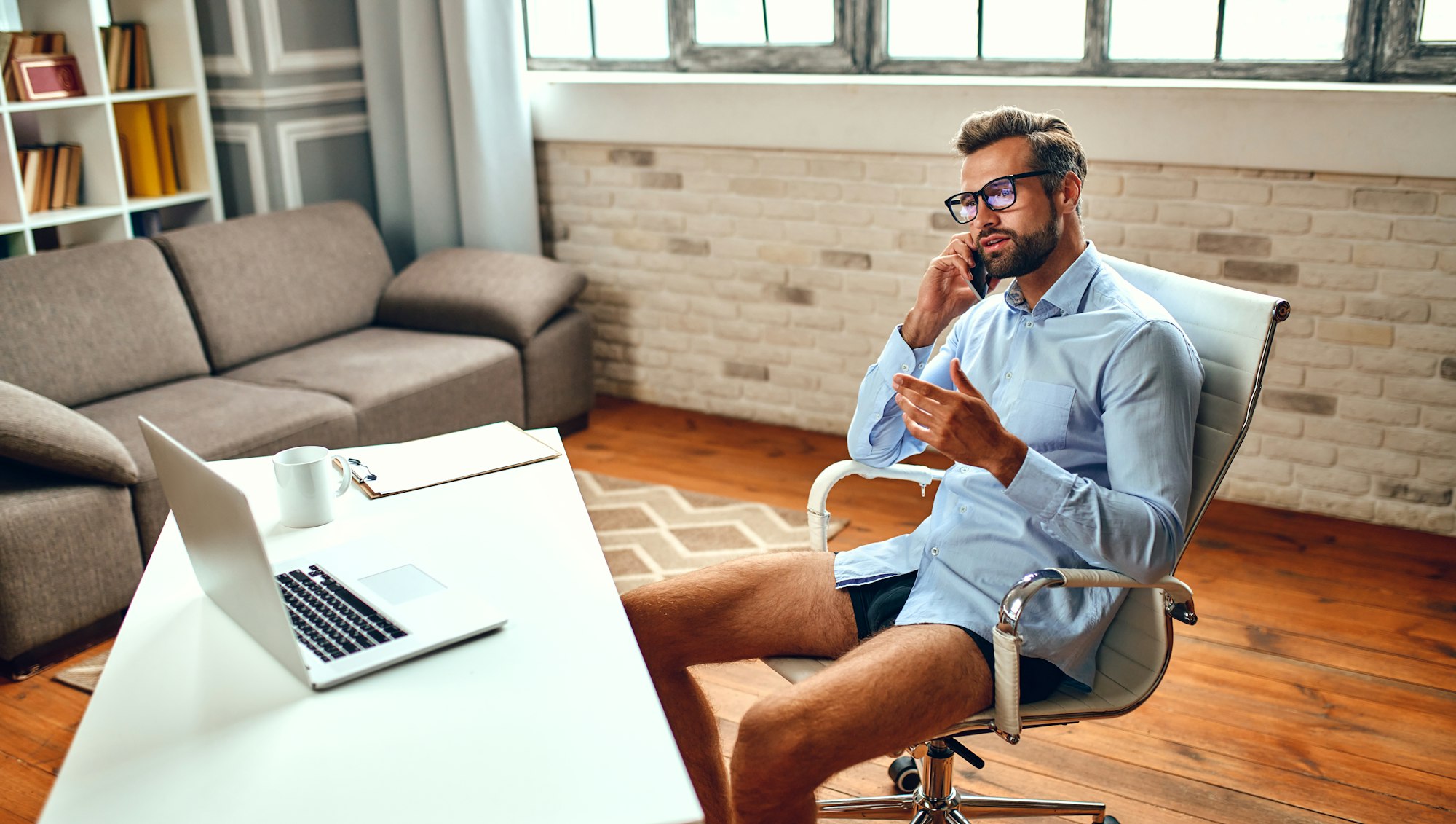 Un bărbat în cămașă și pantaloni scurți stă la o masă și vorbește la un apel video, o conferință de afaceri online, o întâlnire.