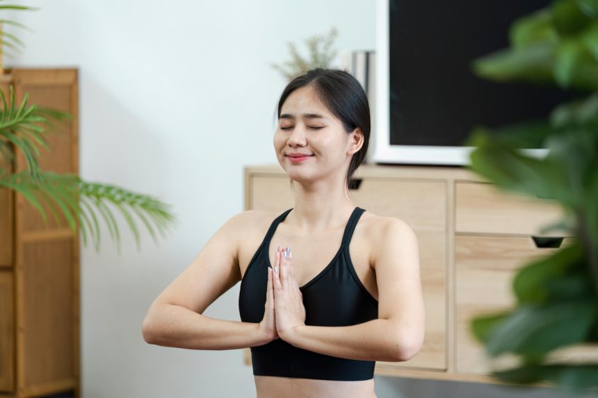 O tânără într-un sutien sport negru care practică yoga și mindfulness acasă, promovând starea de bine și relaxarea.