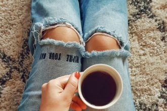 Femeie în ținută de primăvară ținând o ceașcă de cafea și lalele.