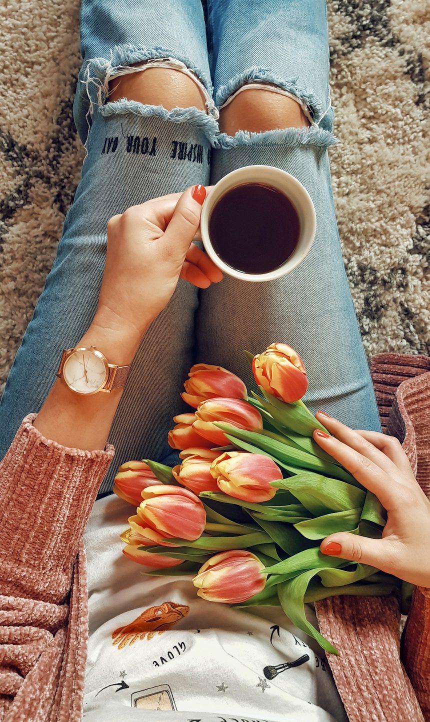Femeie în ținută de primăvară ținând o ceașcă de cafea și lalele.