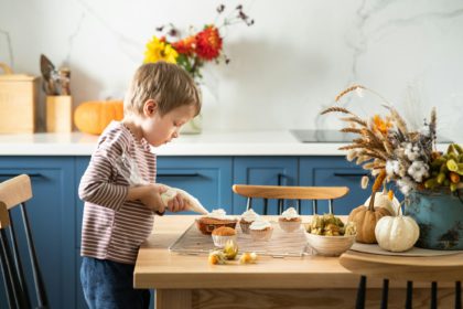 Băiat drăguț care decorează cupcakes cu dovleac cu cremă de brânză și cireșe de iarnă în bucătăria scandinavă