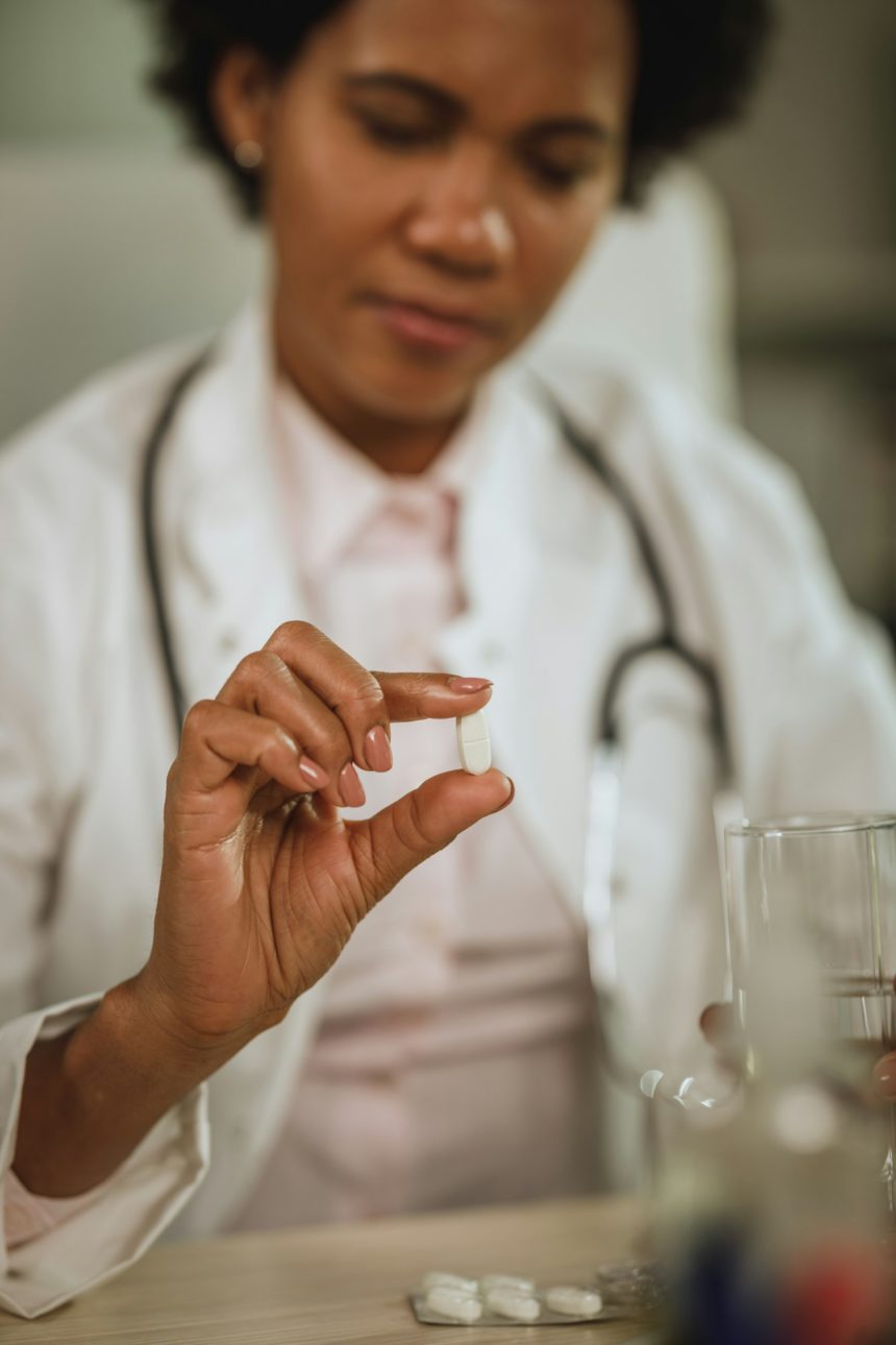 Fotografie cu o doctoriță africană care se simte stresată și ia medicamente în timp ce lucra în biroul ei în timpul pandemiei de COVID-19.