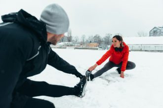 Fotografie cu un cuplu tânăr care se încălzește înainte de alergare într-o zi rece de iarnă