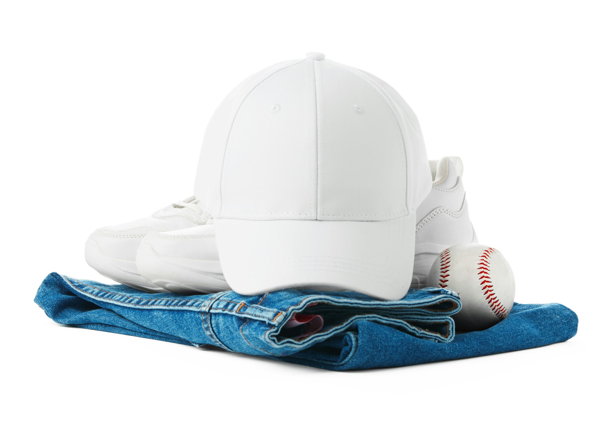 O pereche de pantofi albi și o șapcă de baseball sunt așezate deasupra unei perechi de blugi, creând un ansamblu casual.