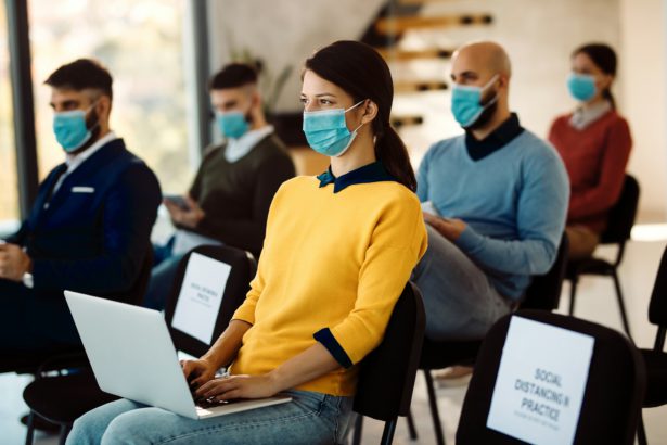 Femeie antreprenor care folosește laptop și poartă mască facială în timp ce participă la o conferință de afaceri în sala de consiliu.