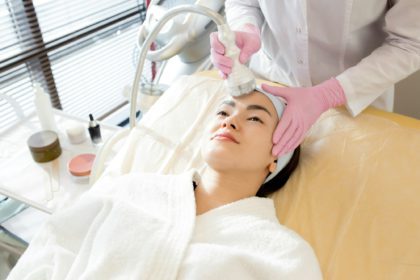 Portret cu unghi înalt al unei femei asiatice drăguțe care se bucură de îngrijire facială în cabinetul cosmetologului, spațiu de copiere