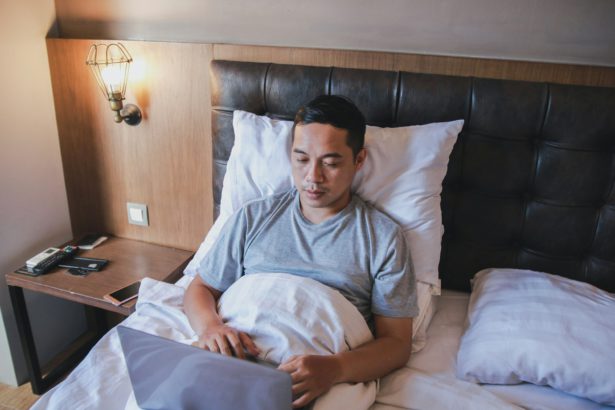 Bărbat serios care lucrează la laptop în timp ce stă pe pat