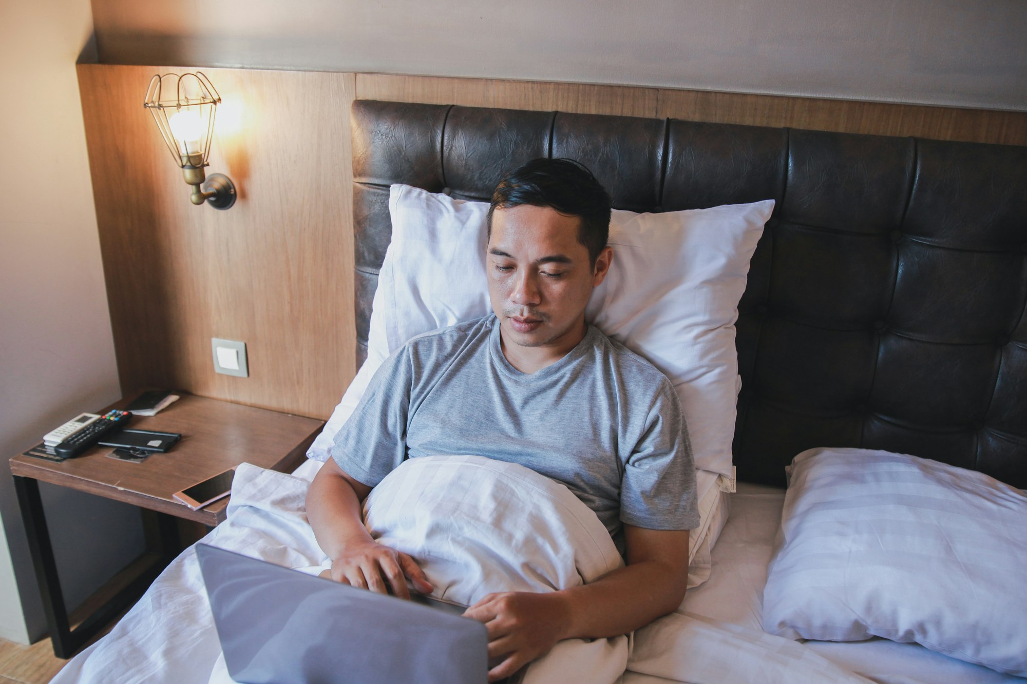 Bărbat serios care lucrează la laptop în timp ce stă pe pat