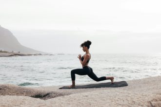 Femeie în îmbrăcăminte de fitness practică yoga pe o saltea la malul mării