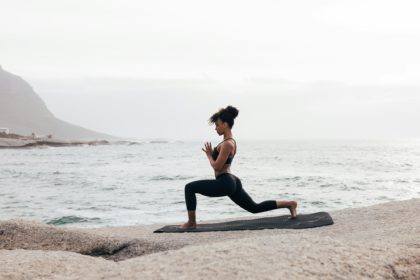 Femeie în îmbrăcăminte de fitness practică yoga pe o saltea la malul mării
