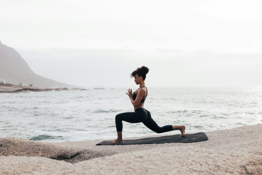 Femeie în îmbrăcăminte de fitness practică yoga pe o saltea la malul mării