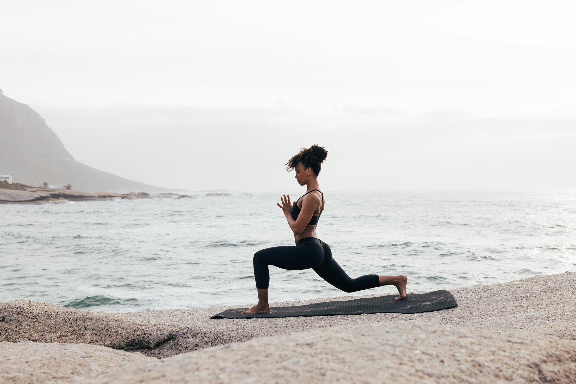 Femeie în îmbrăcăminte de fitness practică yoga pe o saltea la malul mării