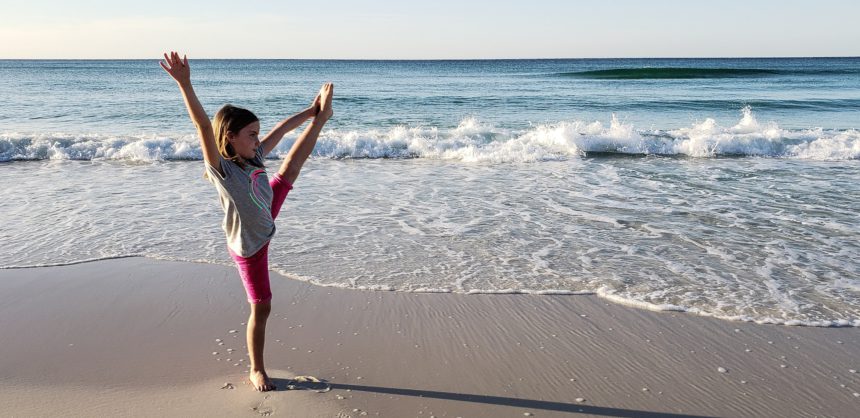 Fata generației z pe plajă făcând yoga și exerciții de întindere de rutină înainte de a merge pe plajă cu valuri oceanului și cer albastru într-un peisaj minimalist al minimalismului.